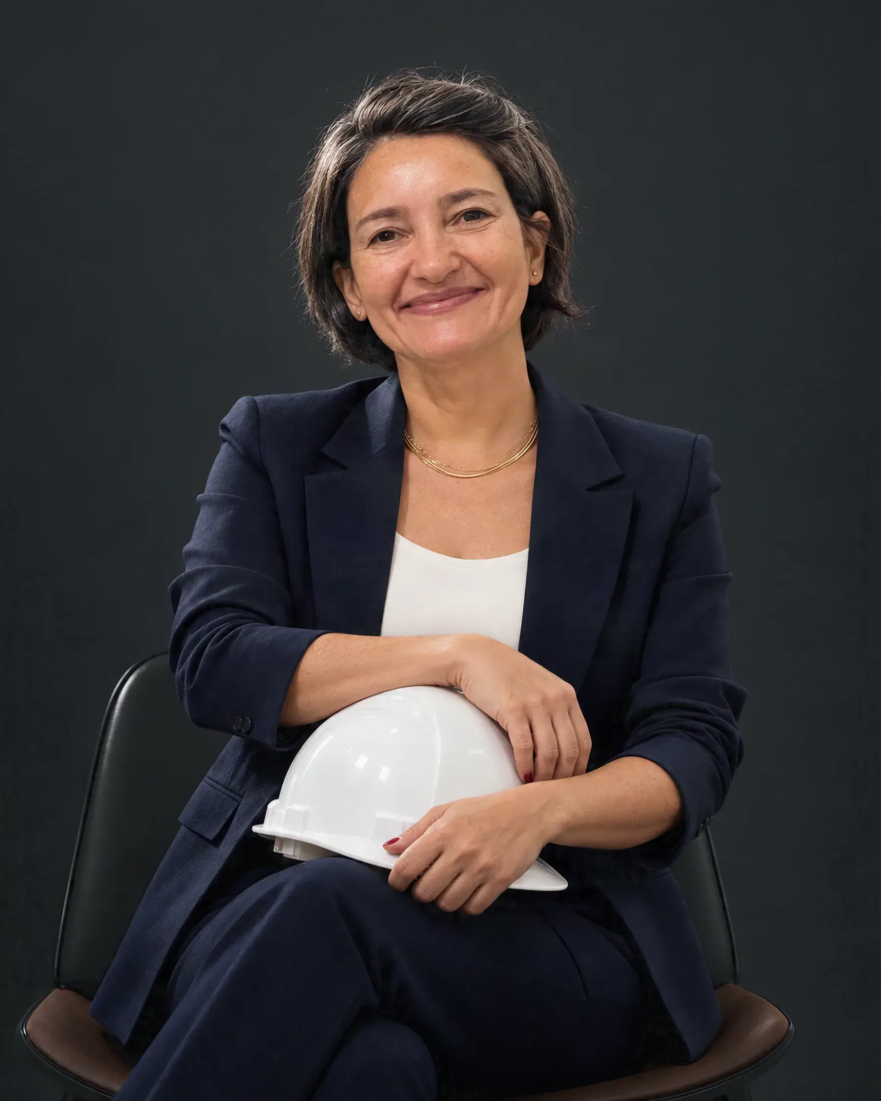 Simone Troina sentada, de terno azul-marinho, com o capacete branco de segurança no colo.